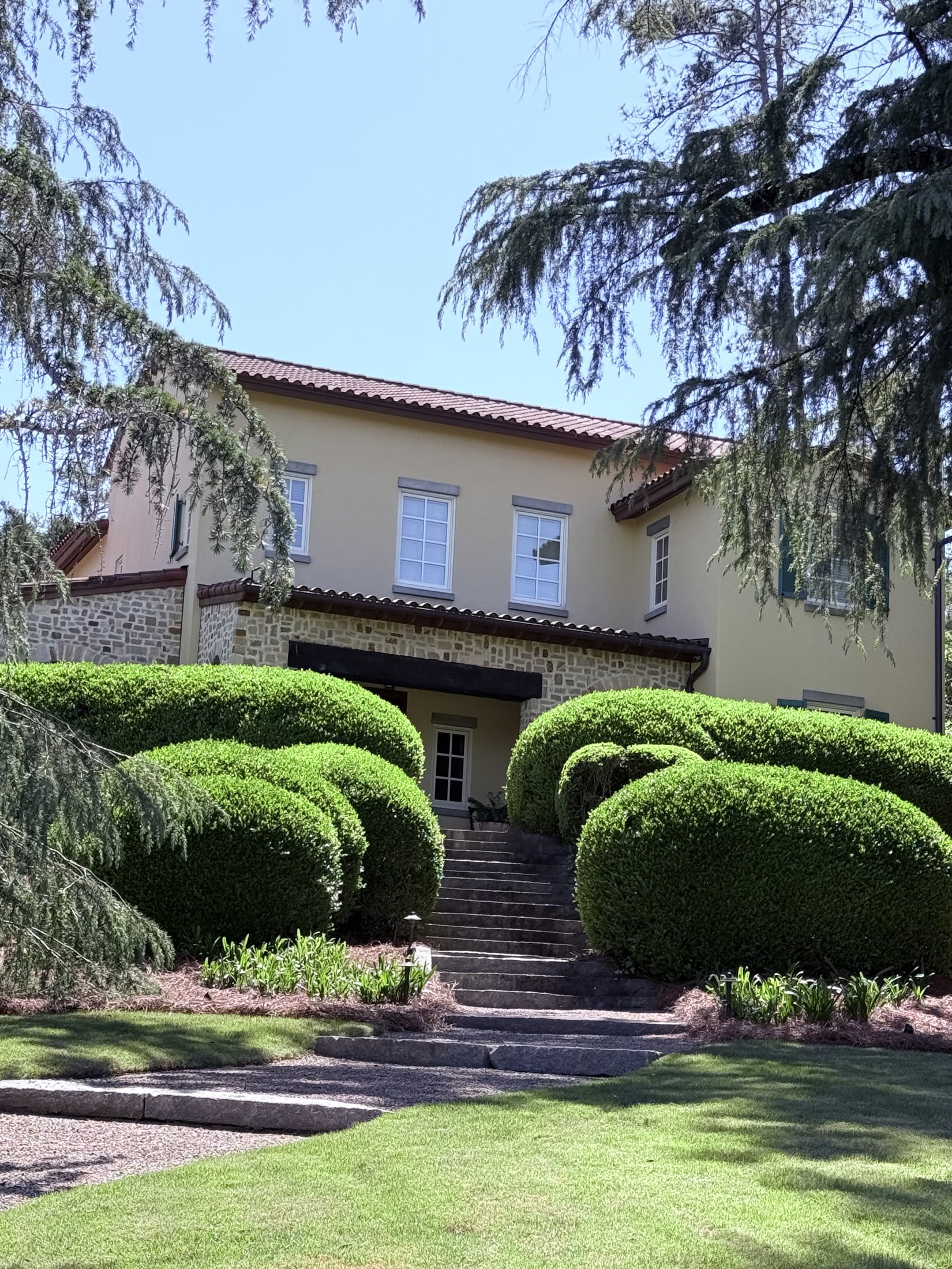Stucco two-story home set behind sculpted rounded boxwood hedges on a sloping lawn, Augusta, Georgia, architectural photography by Nelson White
