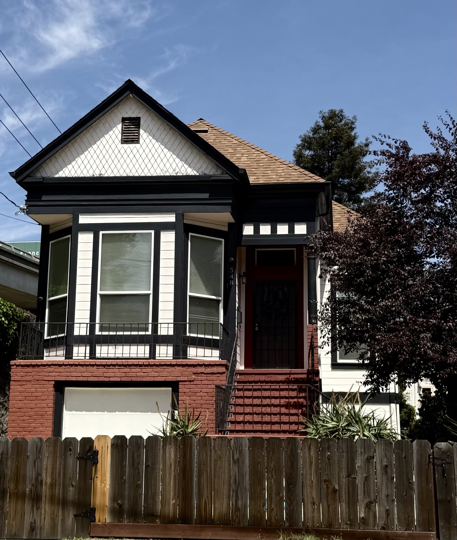 Victorian home with a two-story bay window, dark trim, and brick base behind a wood fence, Bay Area, California, architectural photography by Nelson White